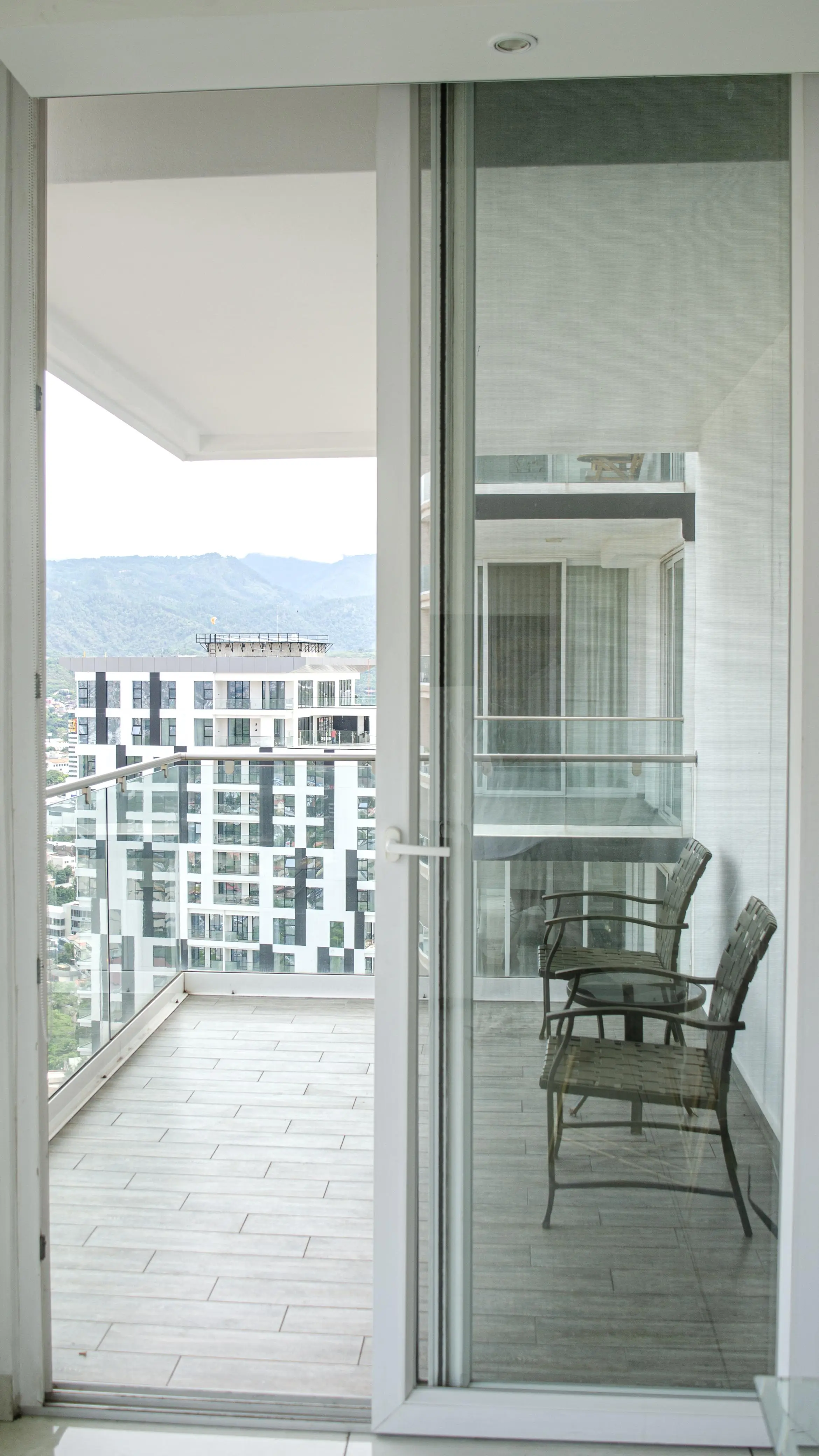 Balcón del piso 12 con dos sillas, piso de madera y vista a los edificios y las montañas.