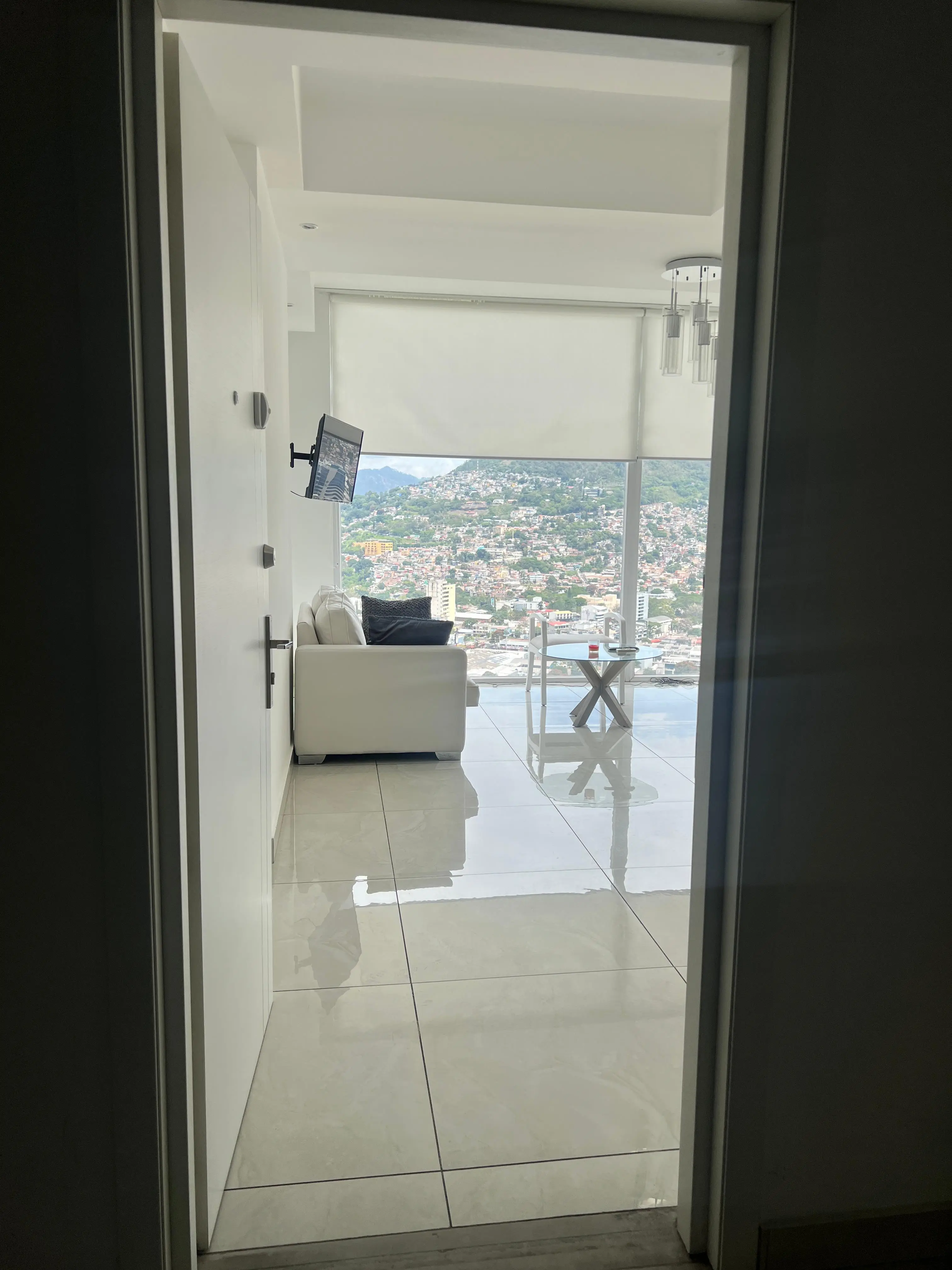 Puerta de entrada abierta hacia la sala, con el ventanal y la ciudad al fondo.
